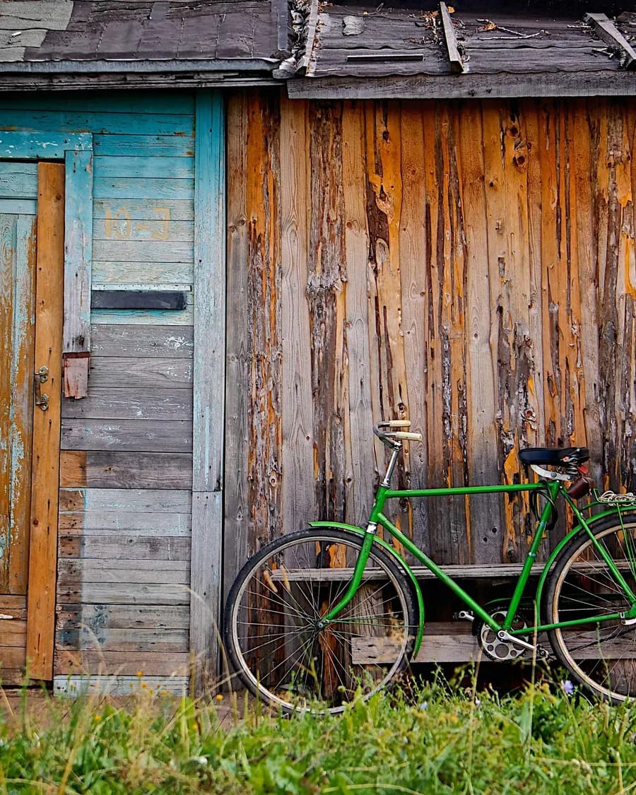 A weathered wooden shed wall with a faded blue door and a green bicycle leaning against it.