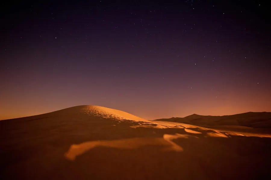 Smooth desert dunes in deep amber tones beneath a dark violet night sky.